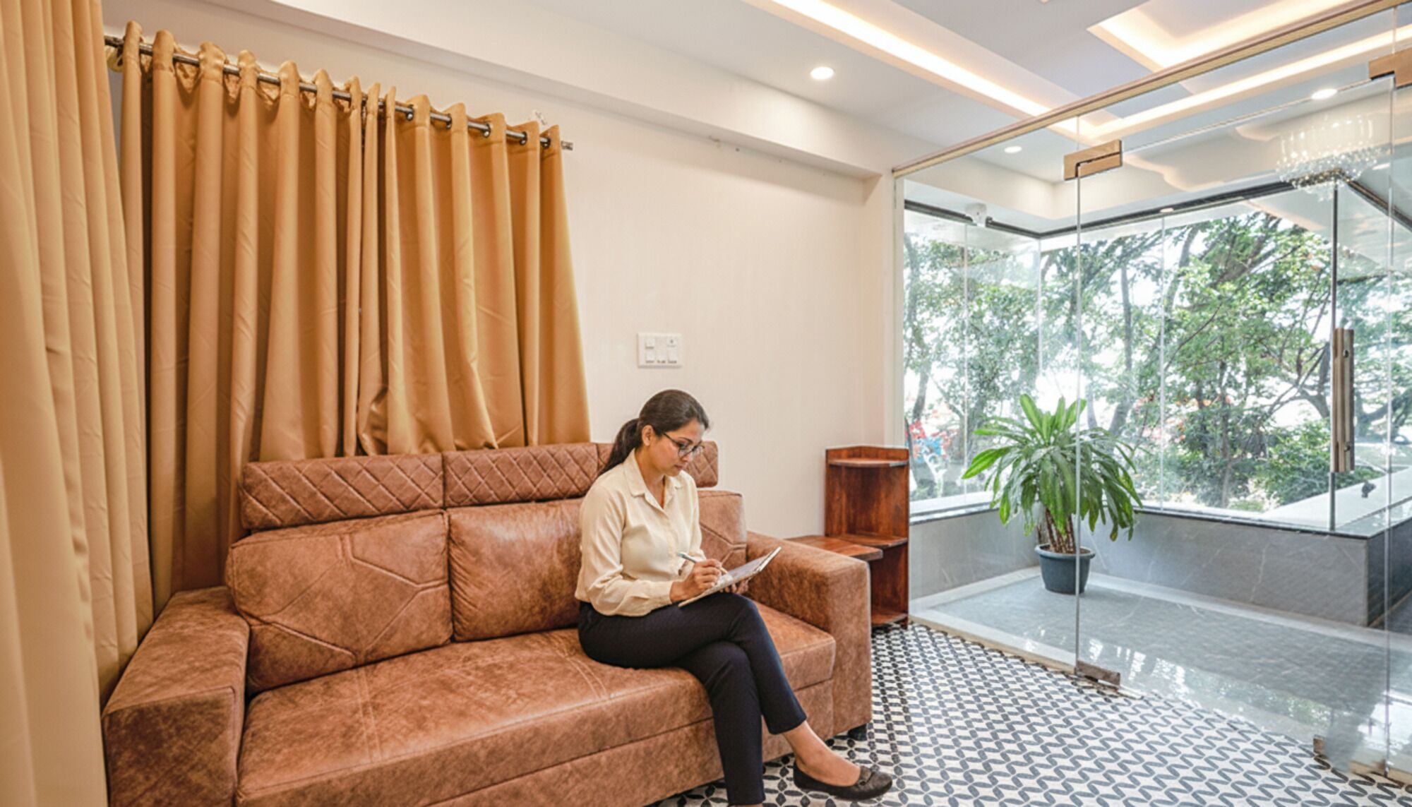 A person sitting on a brown leather sofa in a modern lobby with a glass door leading outside.