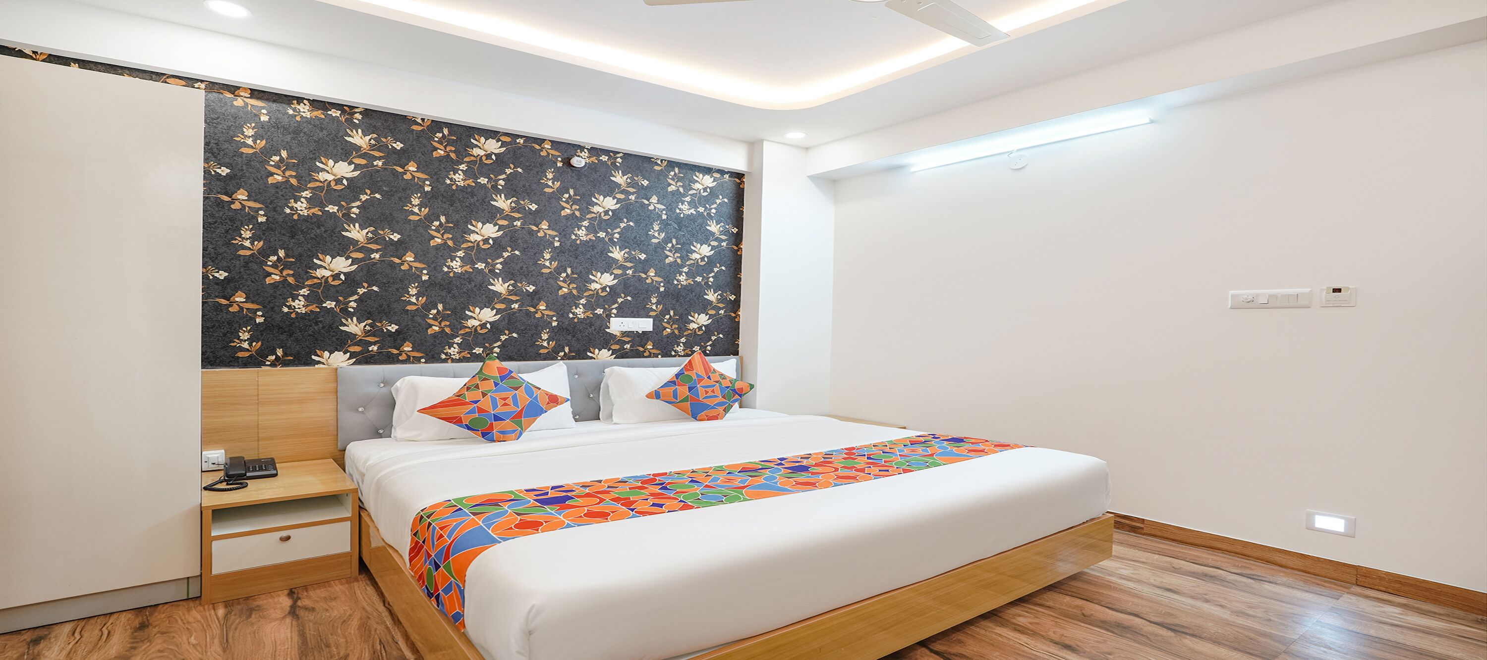 Ein modernes Schlafzimmer mit einem Bett, einem Nachttisch, einem Schreibtisch und einer Wand mit floralem Muster.