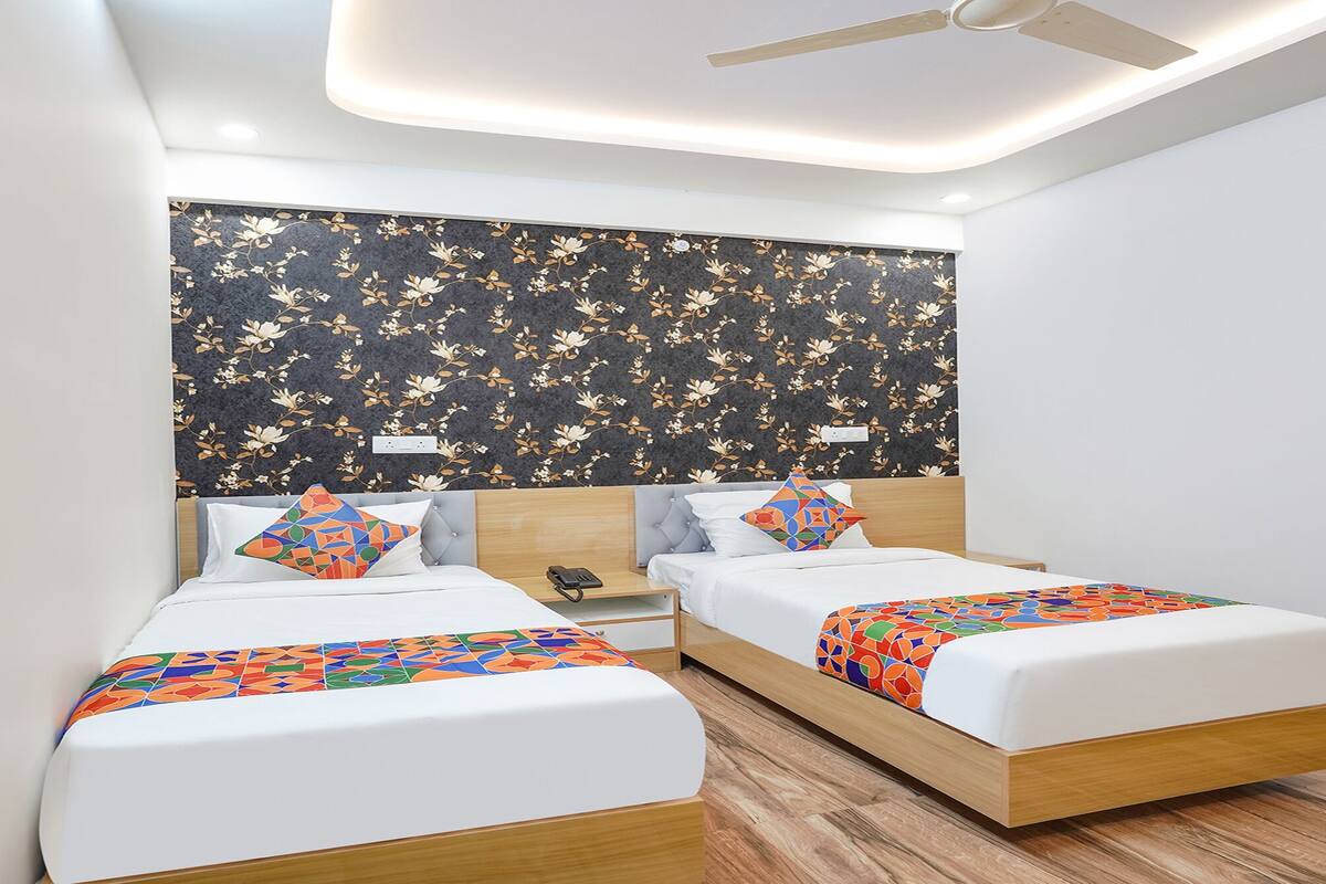 Ein modernes Hotelzimmer mit zwei Einzelbetten, einem Holz-Kopfteil, einer Wand mit floralem Muster und einem Deckenventilator.