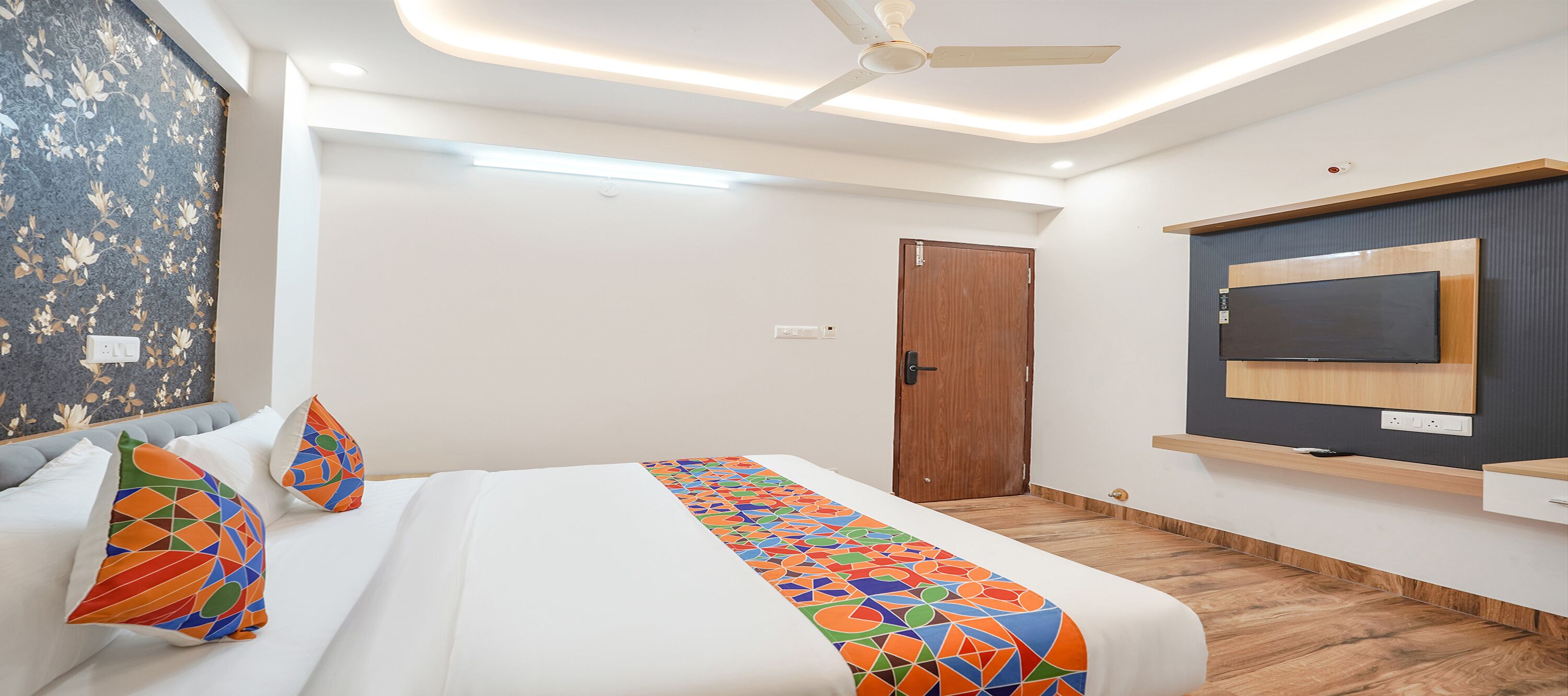 A modern hotel room with a bed, a TV mounted on the wall, and a ceiling fan.