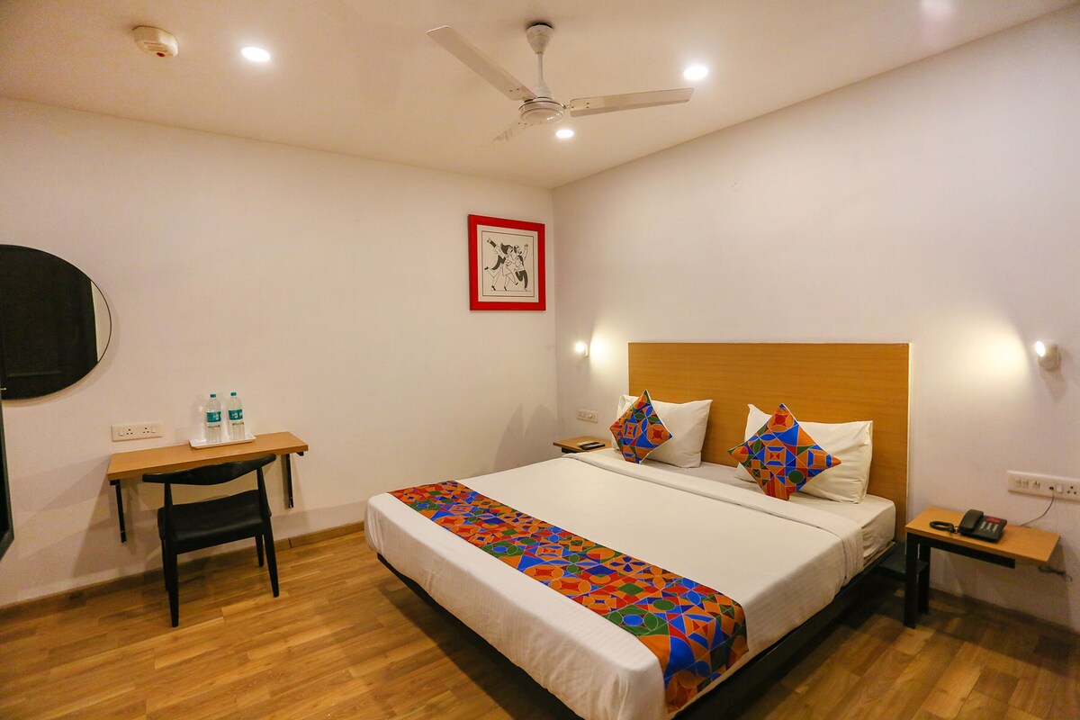 A hotel room with a bed, a desk, a chair, a ceiling fan, and a wall-mounted TV.