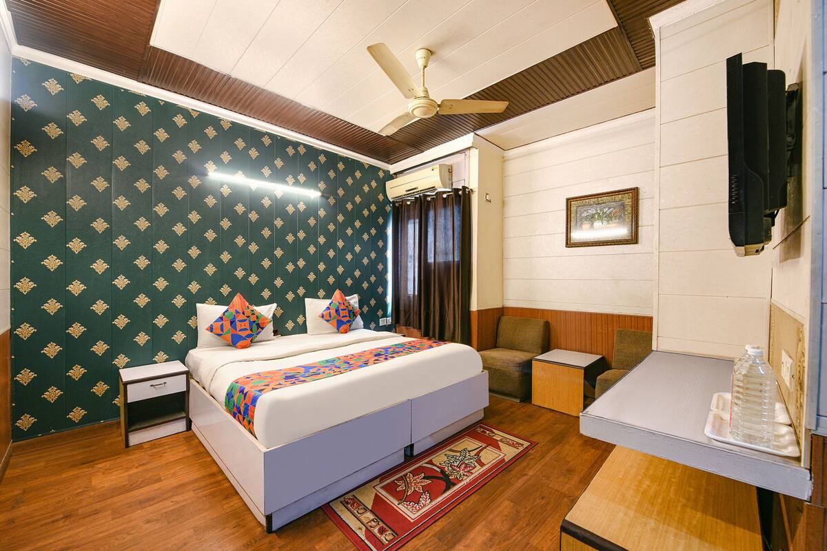 Habitación de hotel con cama, escritorio, silla, mesita de noche, ventilador de techo y televisor.