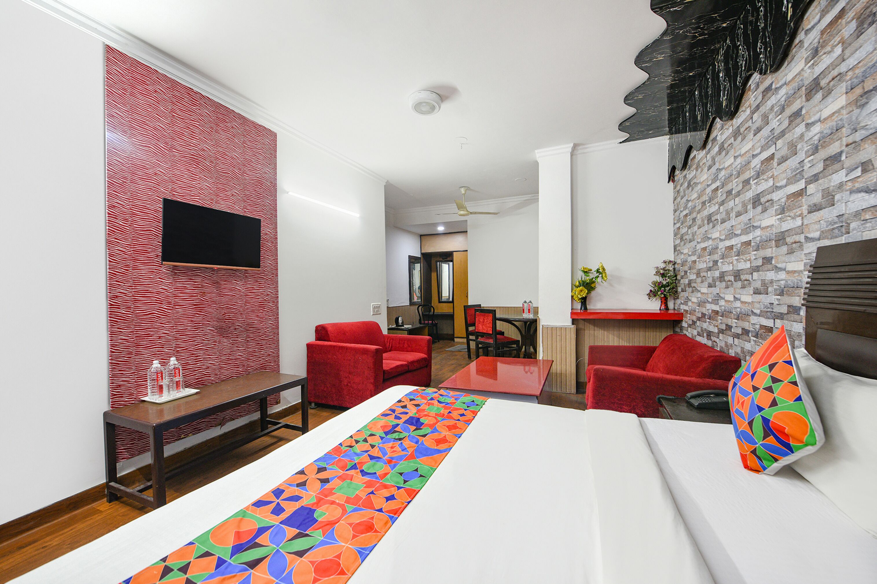 Une chambre d’hôtel avec un grand lit, un téléviseur fixé au mur, un canapé rouge et un coin repas à l’arrière-plan.