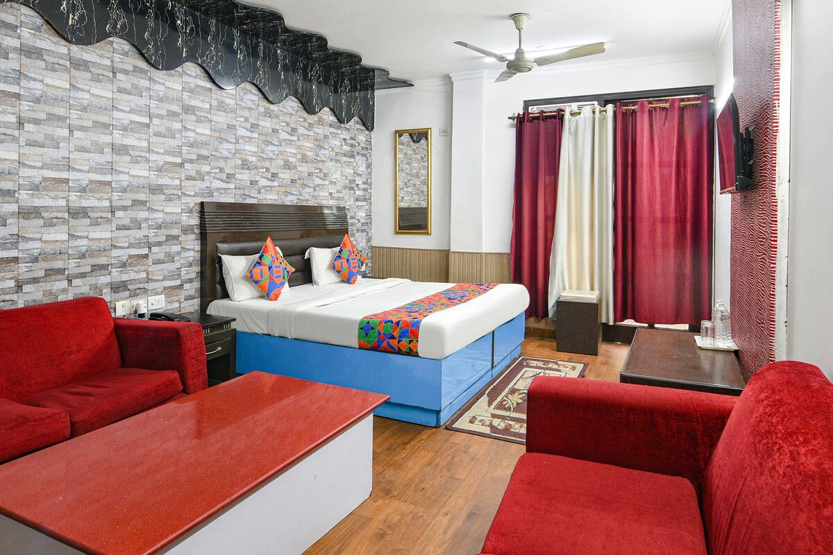 Habitación de hotel con una cama, sofás rojos, una mesita pequeña, un ventilador de techo y un papel tapiz estampado.