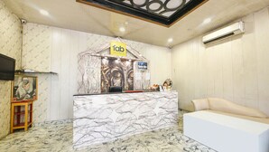 A hotel reception area with a marble reception desk, a sofa, and a wall-mounted air conditioner. - Fabhotel The Icon (New Delhi)
