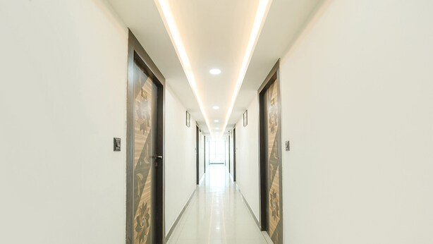 A long, well-lit hallway with doors on either side, leading to a bright room at the end. - Fabhotel Royal Carpet (Patna)