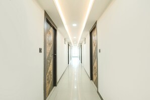 A long, well-lit hallway with doors on either side, leading to a bright room at the end. - Fabhotel Royal Carpet (Patna)