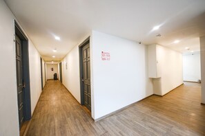 A hotel corridor with wooden flooring, white walls, and doors leading to rooms numbered 101-108 and 109-117. - Fabhotel Crown Inn (Faridabad)