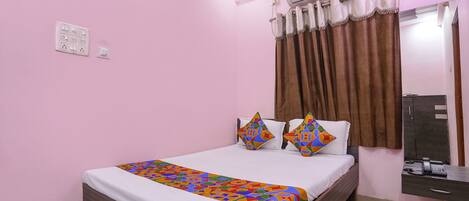 A bedroom with a bed, a bedside table, an air conditioning unit, a telephone, and a mirror.