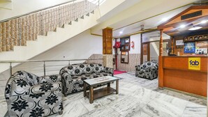 Un hall d’hôtel avec un escalier, des canapés à motifs, un comptoir d’accueil et un sol en marbre.