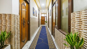 Un couloir aux murs ornés de motifs, avec un tapis bleu et des portes en bois.