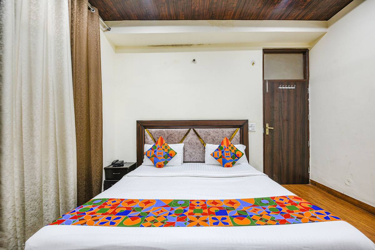 A hotel room with a bed, a nightstand, a wooden door, and a window.