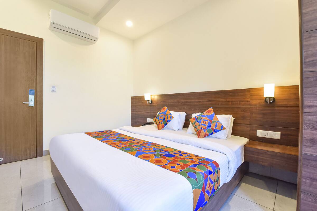 A hotel room with a large bed, a wooden headboard, two wall-mounted lights, and an air conditioning unit.