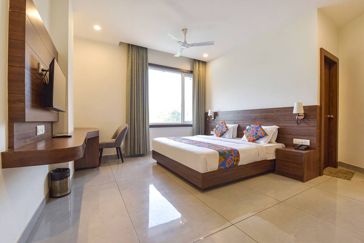 A modern hotel room with a large bed, a desk, a chair, a TV, and a ceiling fan.