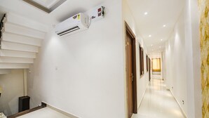 Un couloir d’hôtel avec des murs blancs, une porte en bois et un appareil de climatisation blanc.