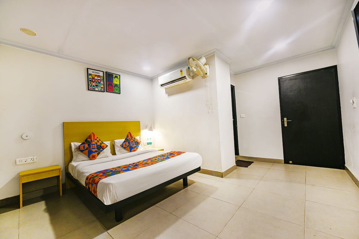 Habitación de hotel con cama, mesita de noche, unidad de aire acondicionado, puerta y aplique de pared.