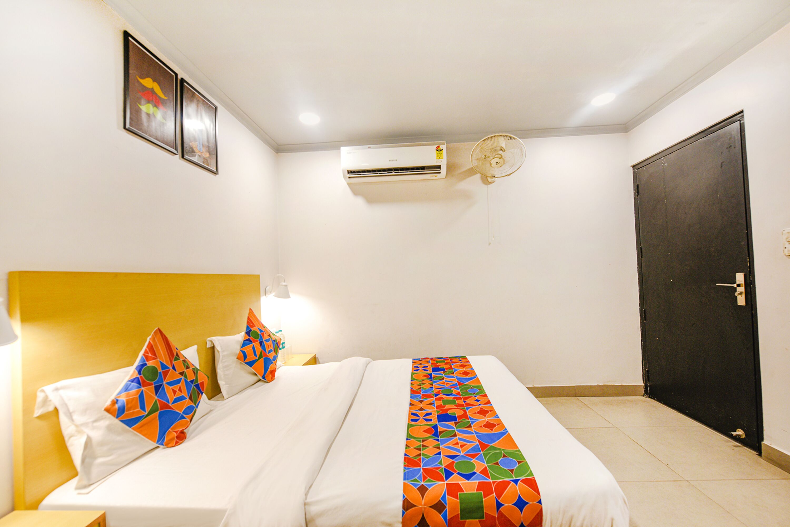 A hotel room with a bed, a nightstand, a wall-mounted air conditioner, and a door.