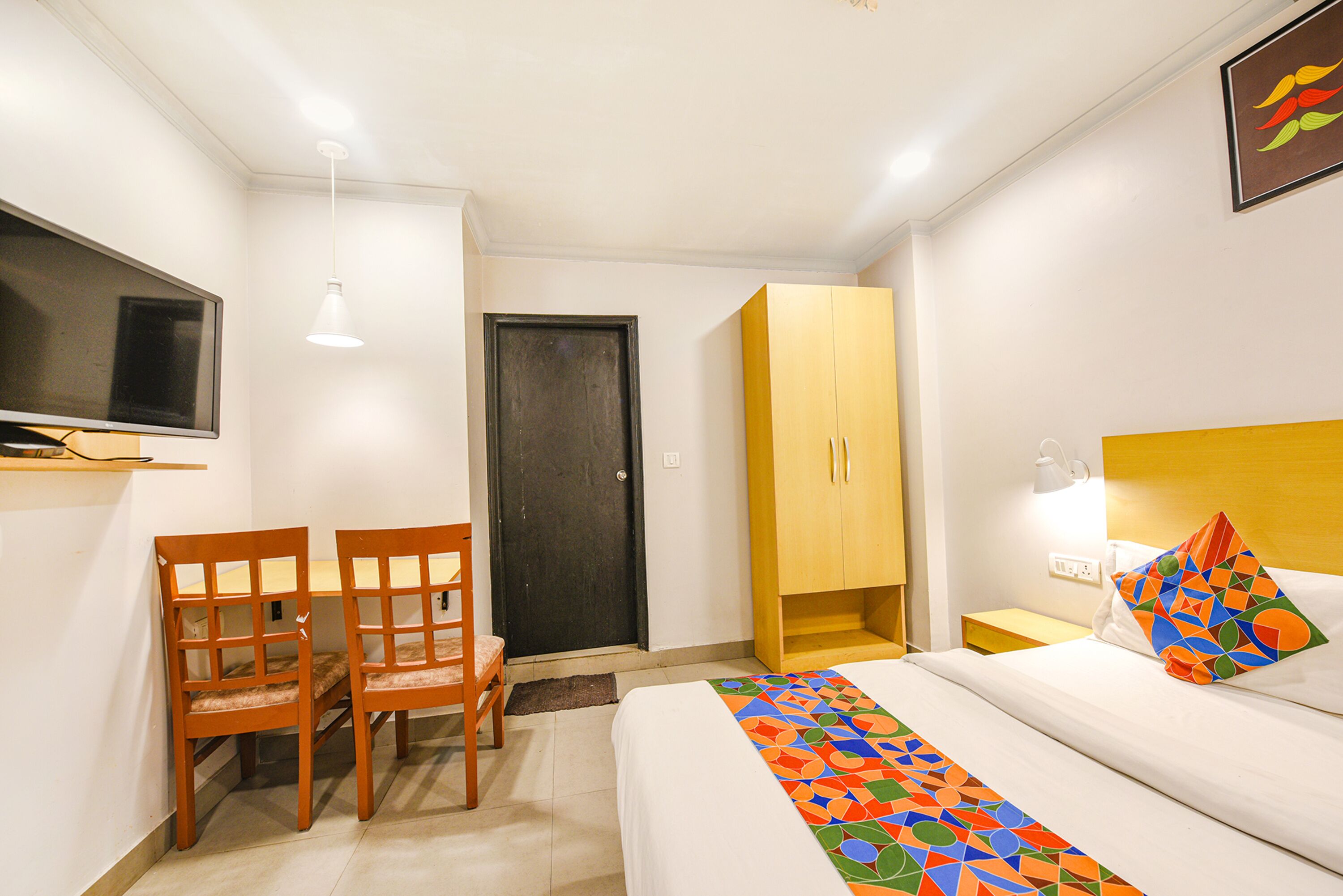 A hotel room with a bed, a desk with chairs, a wardrobe, a television, and a door.