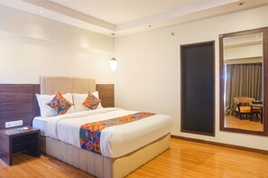 A hotel room with a large bed, a nightstand, a mirror, and a wooden floor. - Oriva Mapple By Supriya (Pune)