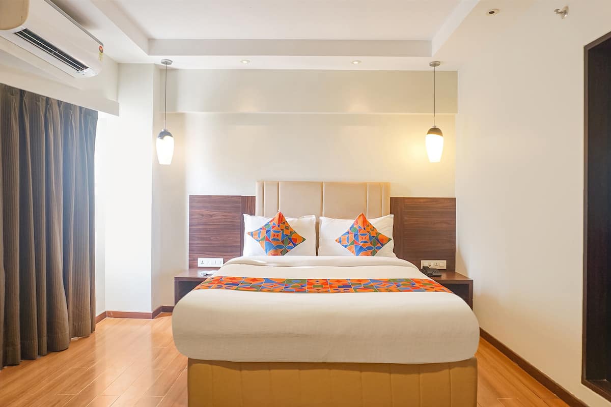 Habitación de hotel con una cama grande, dos mesitas de noche, una lámpara de noche, una ventana con cortinas y aire acondicionado instalado en el techo.