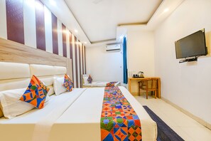 Una habitación de hotel con una cama grande, un televisor montado en la pared y un escritorio con una silla.