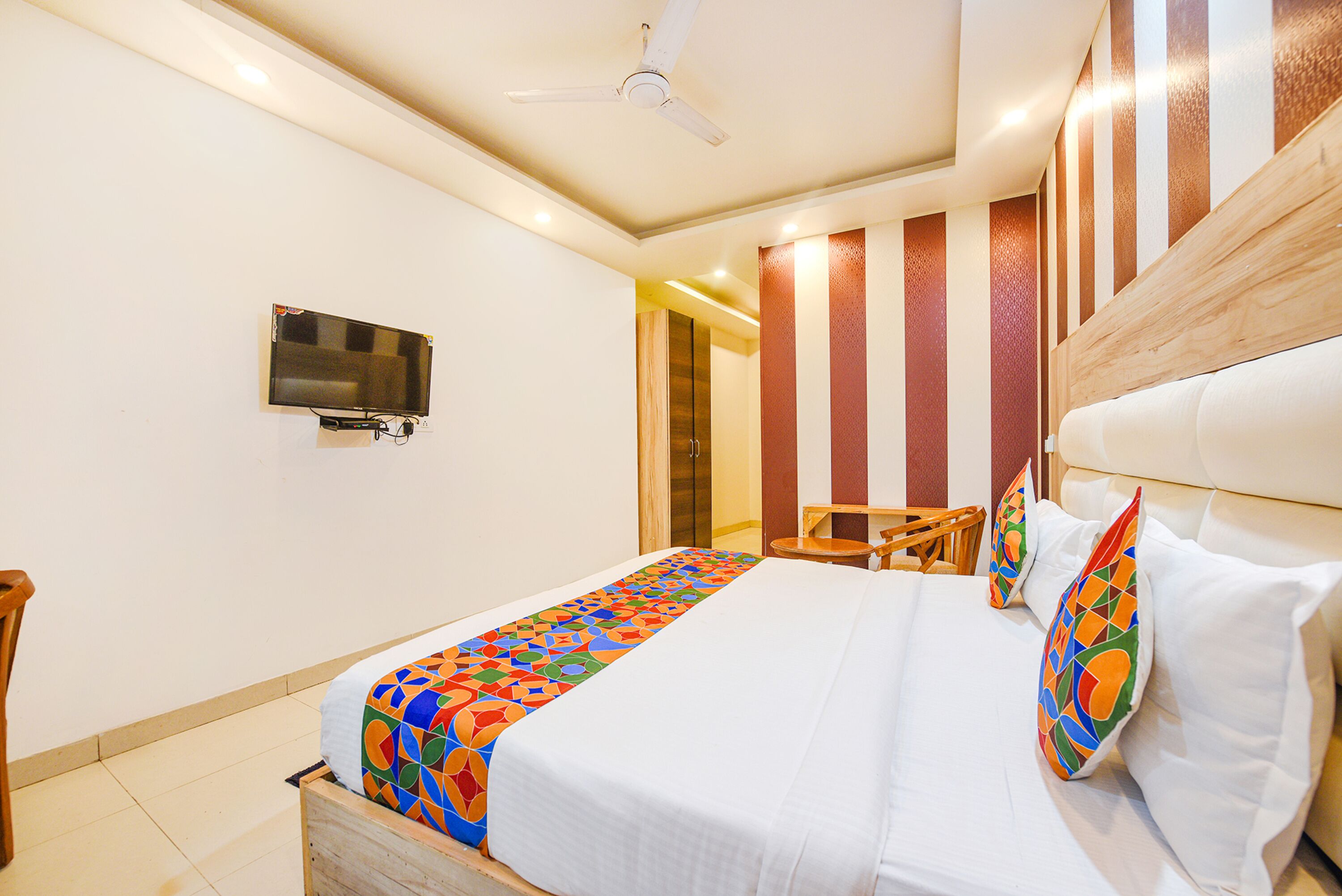 A hotel room with a bed, a TV mounted on the wall, and a ceiling fan.