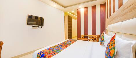 A hotel room with a bed, a TV mounted on the wall, and a ceiling fan.