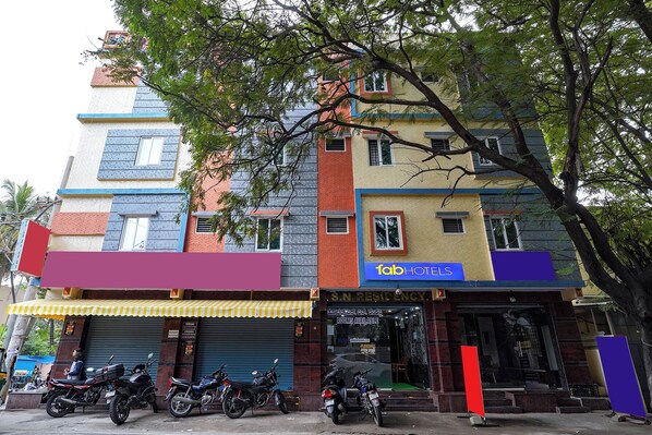 Egy többemeletes épület, színes homlokzattal, jól látható „fab hotels” felirattal, és számos parkoló motorkerékpárral az előtte.