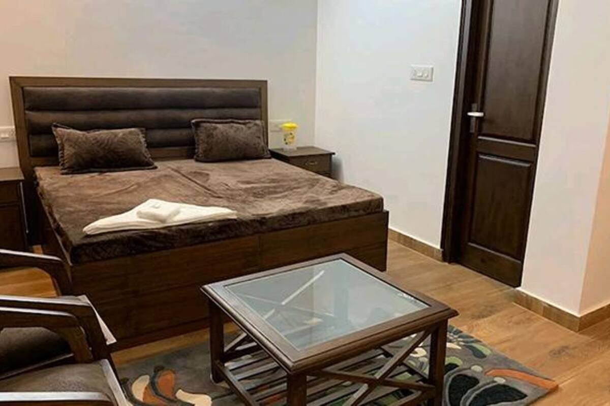 A bedroom with a bed, a bedside table, a glass-top table, and a door.
