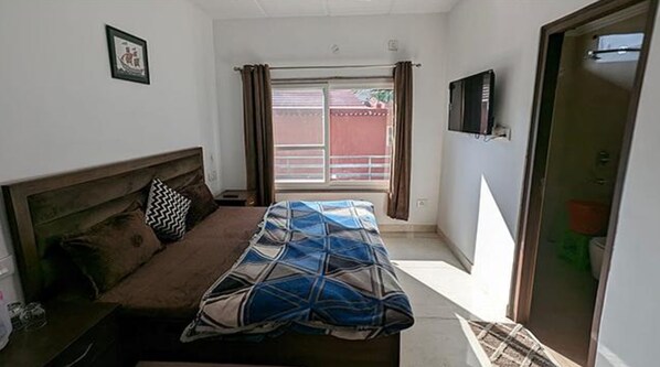 Un dormitorio con cama, cabecera, ventana con cortinas, televisión en la pared y puerta.