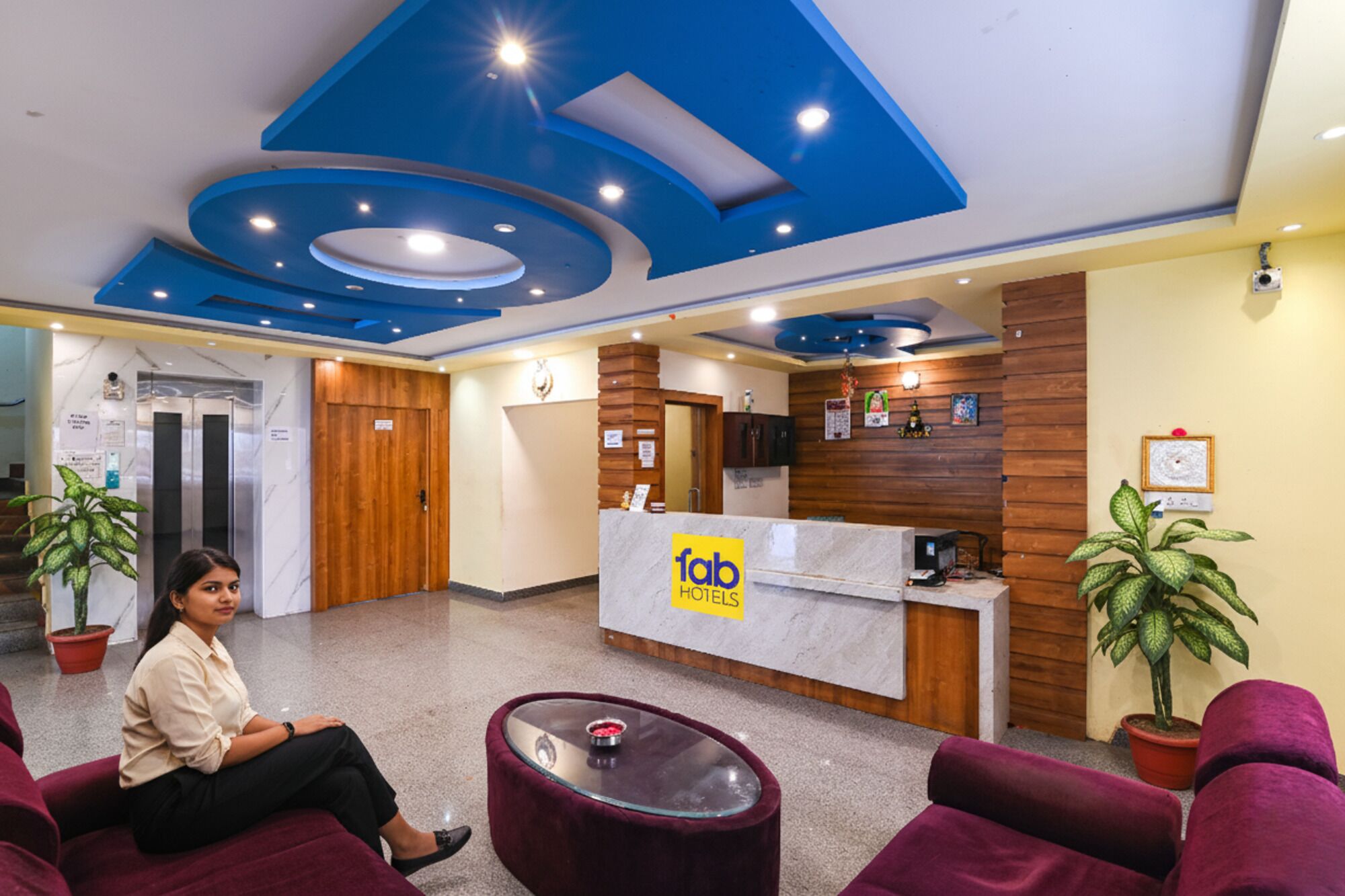 A hotel reception area with a modern design, including a blue ceiling, a reception desk labeled 'Tab Hotels', and a seating area with red sofas.