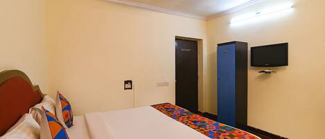 A hotel room with a bed, a ceiling fan, a TV mounted on the wall, and a door.