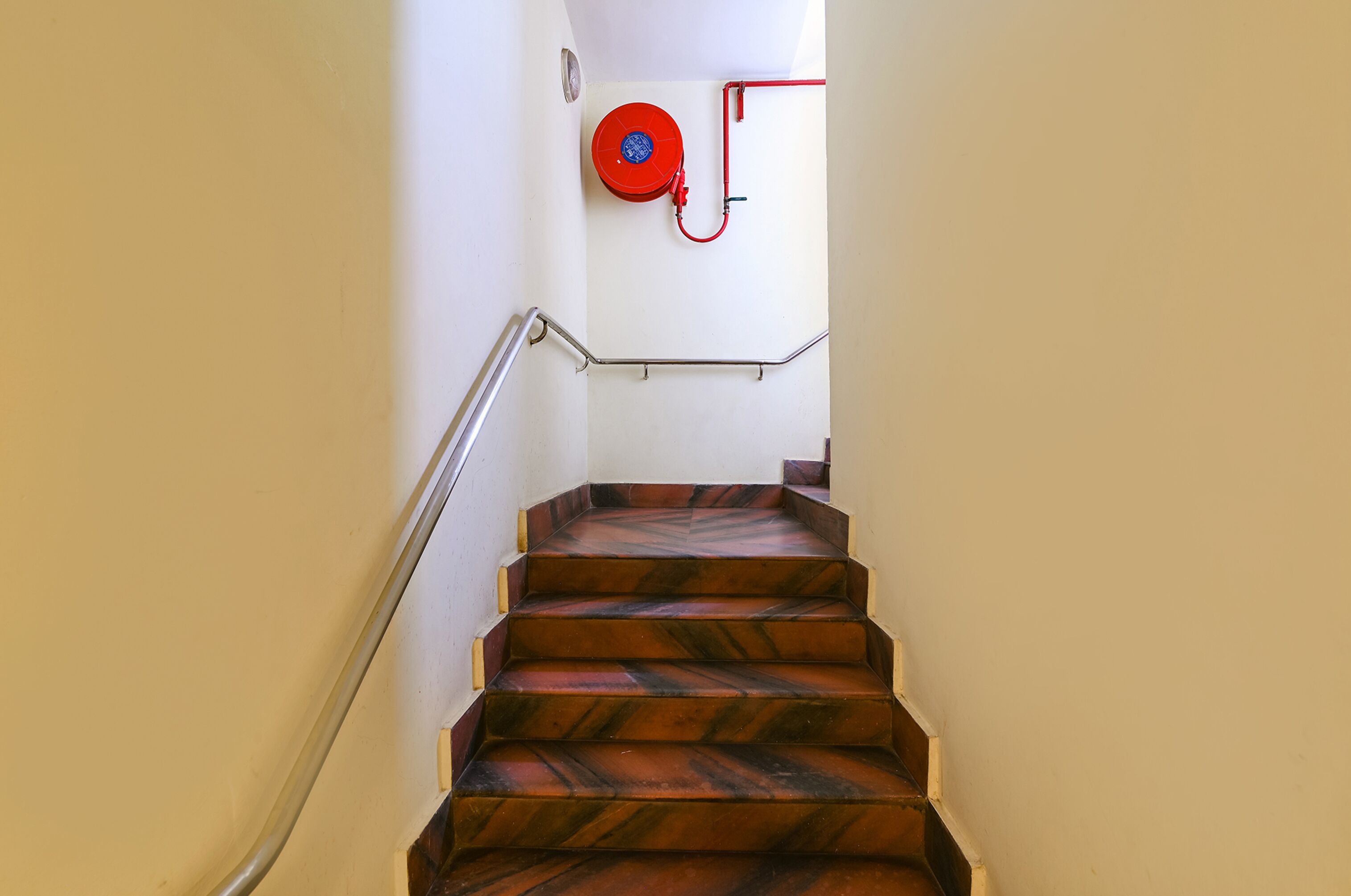 A staircase with a metal handrail and a red fire hose reel mounted on the wall.