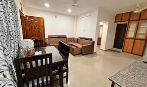 A living room with a sectional sofa, a dining table with chairs, and a kitchen area with wooden cabinets.