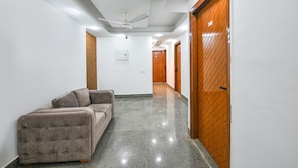 A hallway with a sofa, wooden doors, and a ceiling fan. - FabHotel The Cozy Cloud (New Delhi)