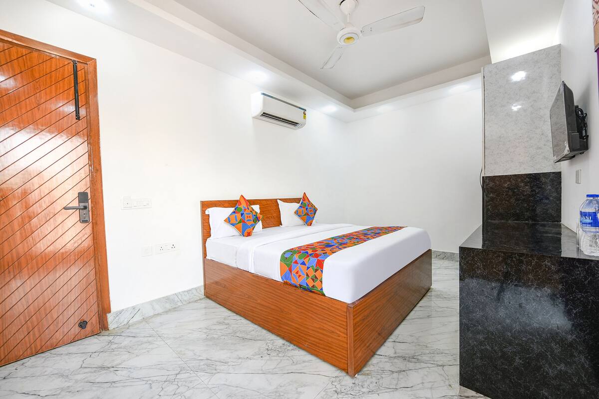 A hotel room with a wooden bed, white walls, a ceiling fan, an air conditioning unit, a marble floor, and a black marble counter.