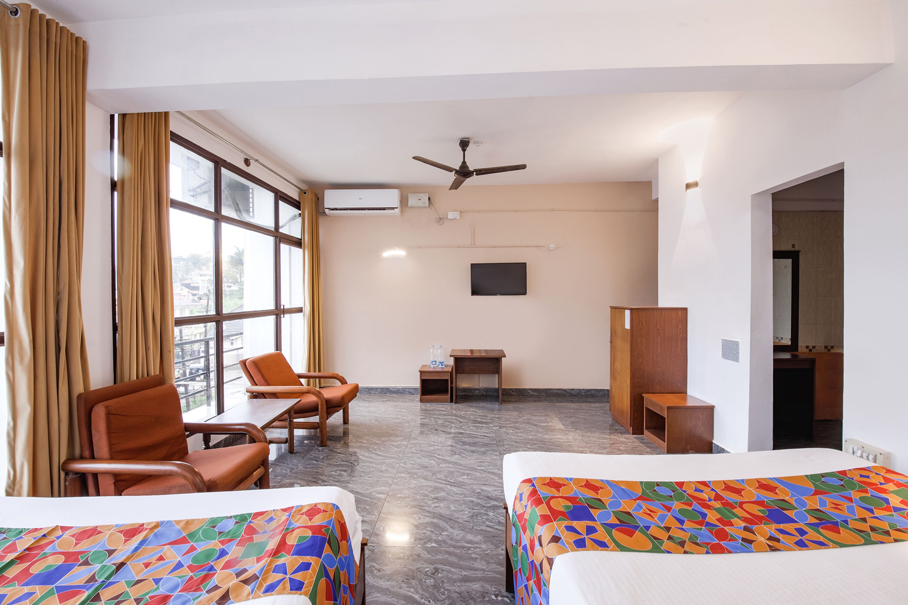 Habitación de hotel con dos camas, un escritorio, una silla, un televisor y un ventilador de techo.