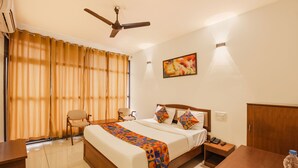 A hotel room with a bed, a desk, a chair, a ceiling fan, and a painting on the wall. - Fabhotel Raj (Madikeri)