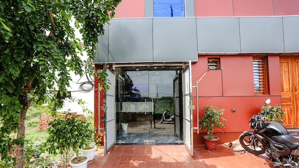 A building entrance with a glass door, potted plants, and a motorcycle parked outside. - Fabhotel Sangita Dham (Mathura)