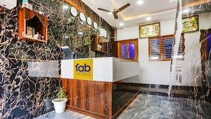A reception desk with a 'fab hotels' sign, marble walls, a wooden reception desk, a ceiling fan, and a potted plant. - Fabhotel Sangita Dham (Mathura)