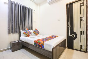 A bedroom with a bed, bedside table, curtains, and a door. - Fabhotel Legacy I (Nagpur)