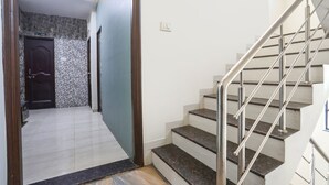Una scala con ringhiere in metallo e pavimento piastrellato che conduce a una stanza con una porta in legno scuro e un muro rivestito di piastrelle.