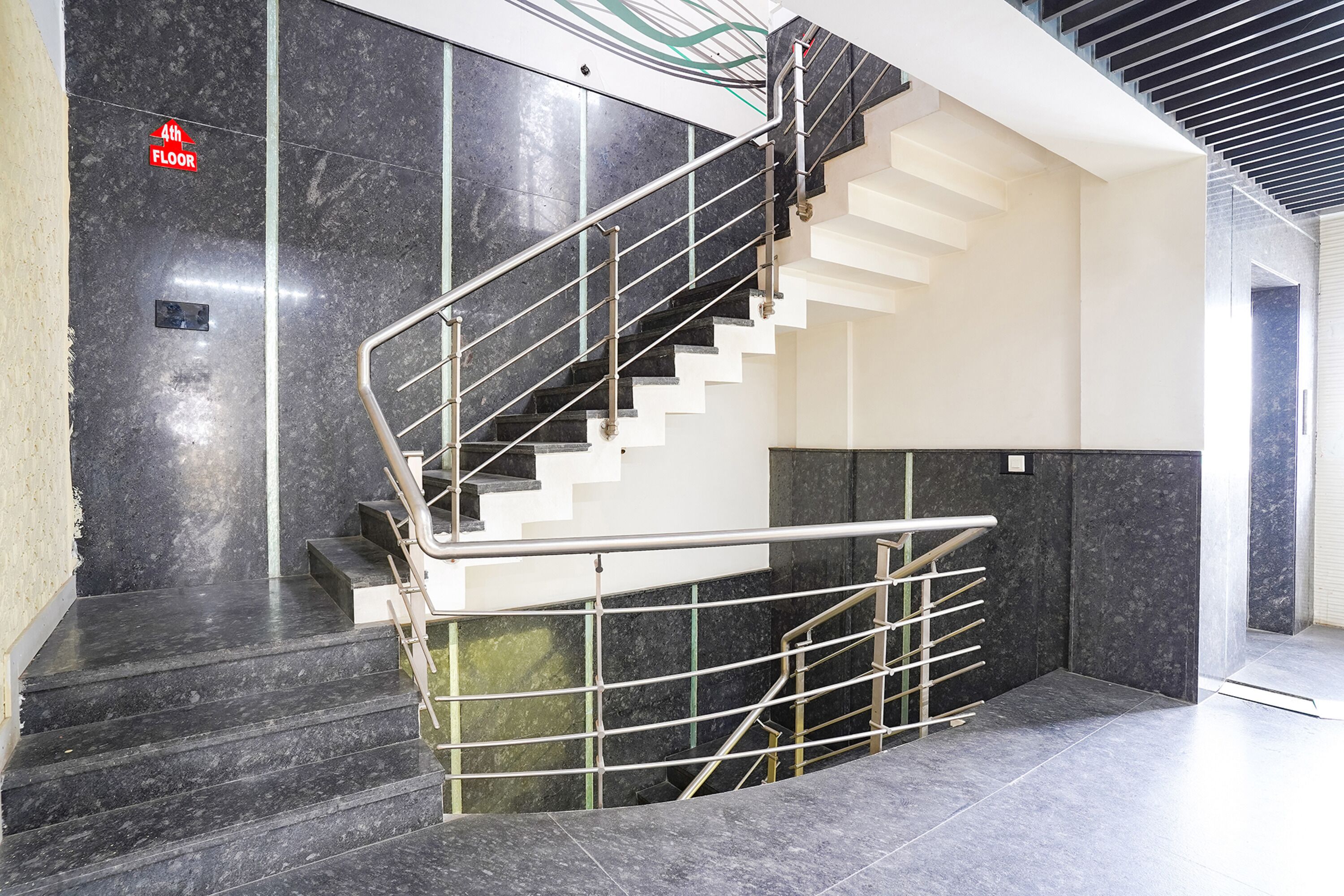 A modern staircase with a metal handrail and black marble steps leading to a 4th floor.