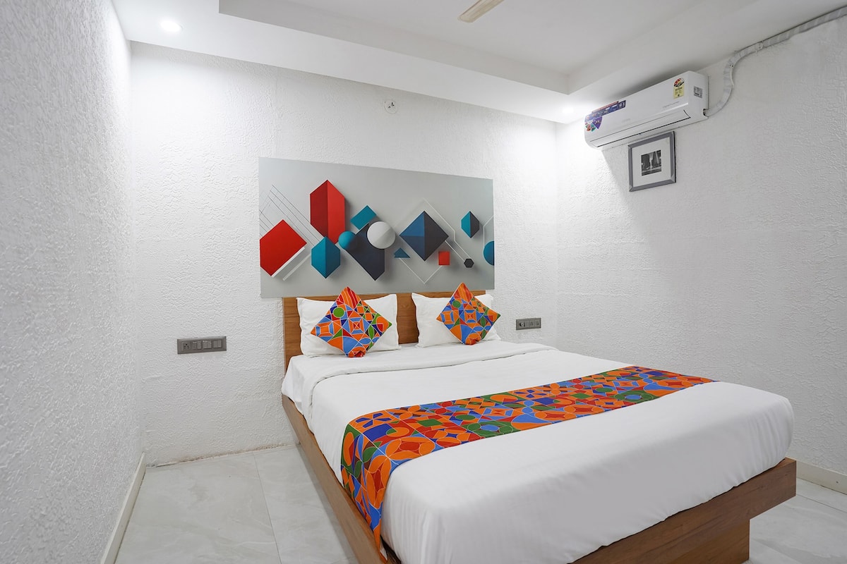 A bedroom with a bed, white walls, a ceiling fan, an air conditioning unit, and a geometric artwork above the bed.