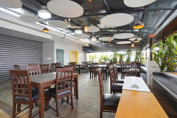 A spacious dining area with multiple tables and chairs, ceiling fans, and pendant lights. - FabExpress NK Comforts (Bengaluru)