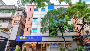 Un edificio de varios pisos con un letrero de 'fab hotels', plantas en macetas y un árbol en la fachada.