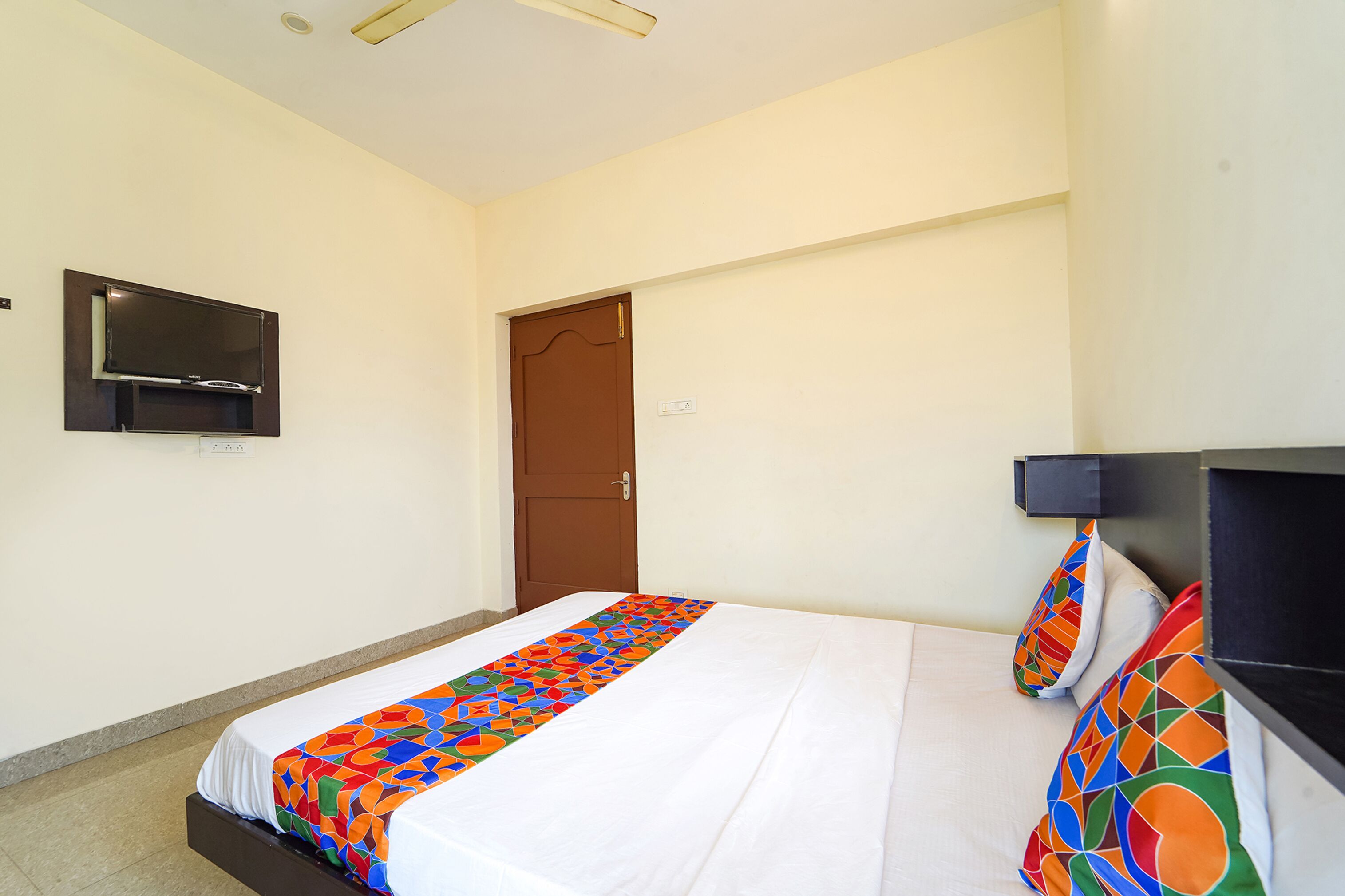 Una habitación de hotel con una cama, un televisor montado en la pared y una puerta.