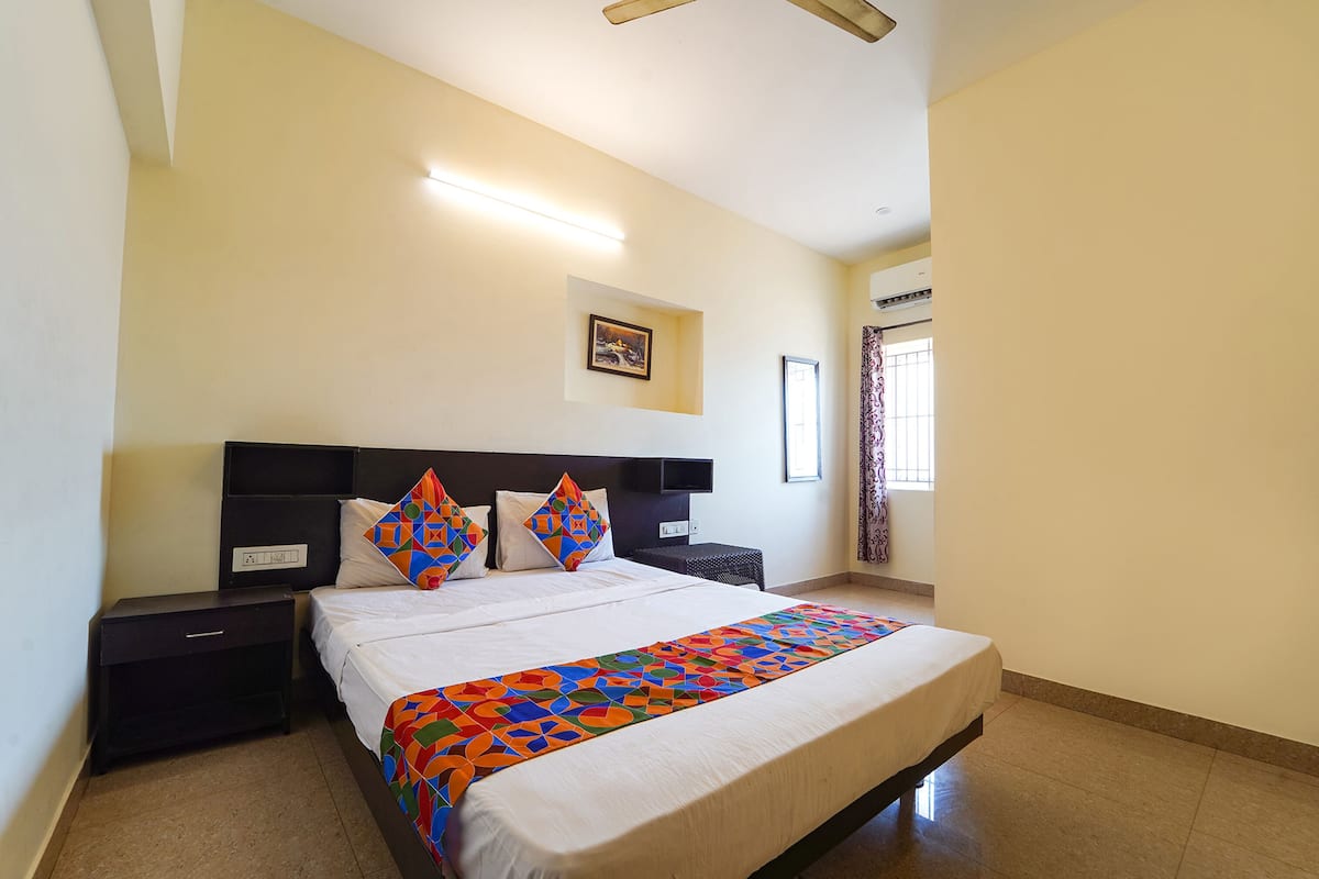 A neatly arranged bedroom with a large bed, a bedside table, a wall-mounted TV, and a window with curtains.