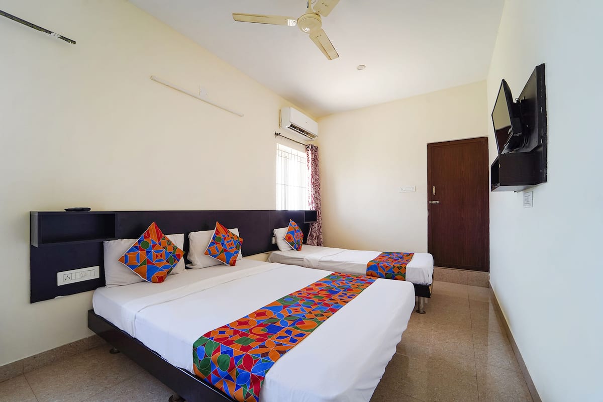 A hotel room with two beds, a ceiling fan, an air conditioning unit, a TV mounted on the wall, and a window with curtains.