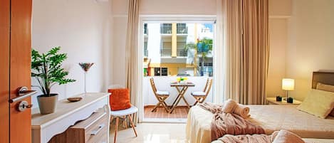 Et hotelværelse med seng, skrivebord, stol, lille bord og en balkon med udsigt til bygninger.